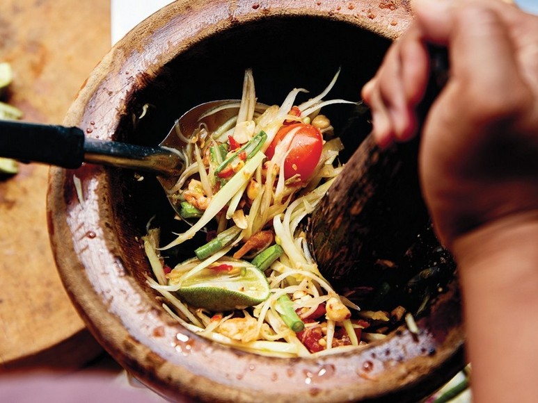 Người bán giã som tum trong cối trước mặt khách