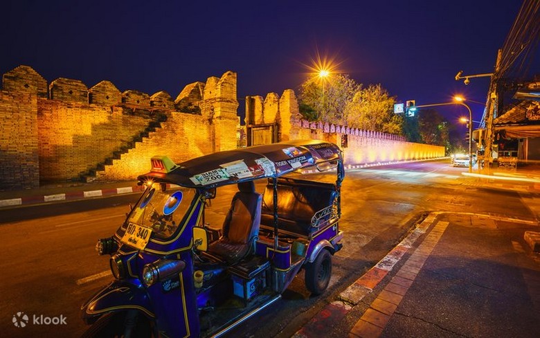 Ảnh tuk-tuk chạy qua con phố cổ Chiang Mai, có ánh đèn vàng buổi tối
