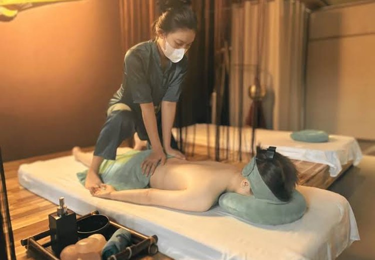 Kỹ thuật viên đang thực hiện động tác kéo giãn lưng cho khách trong không gian tiệm massage truyền thống